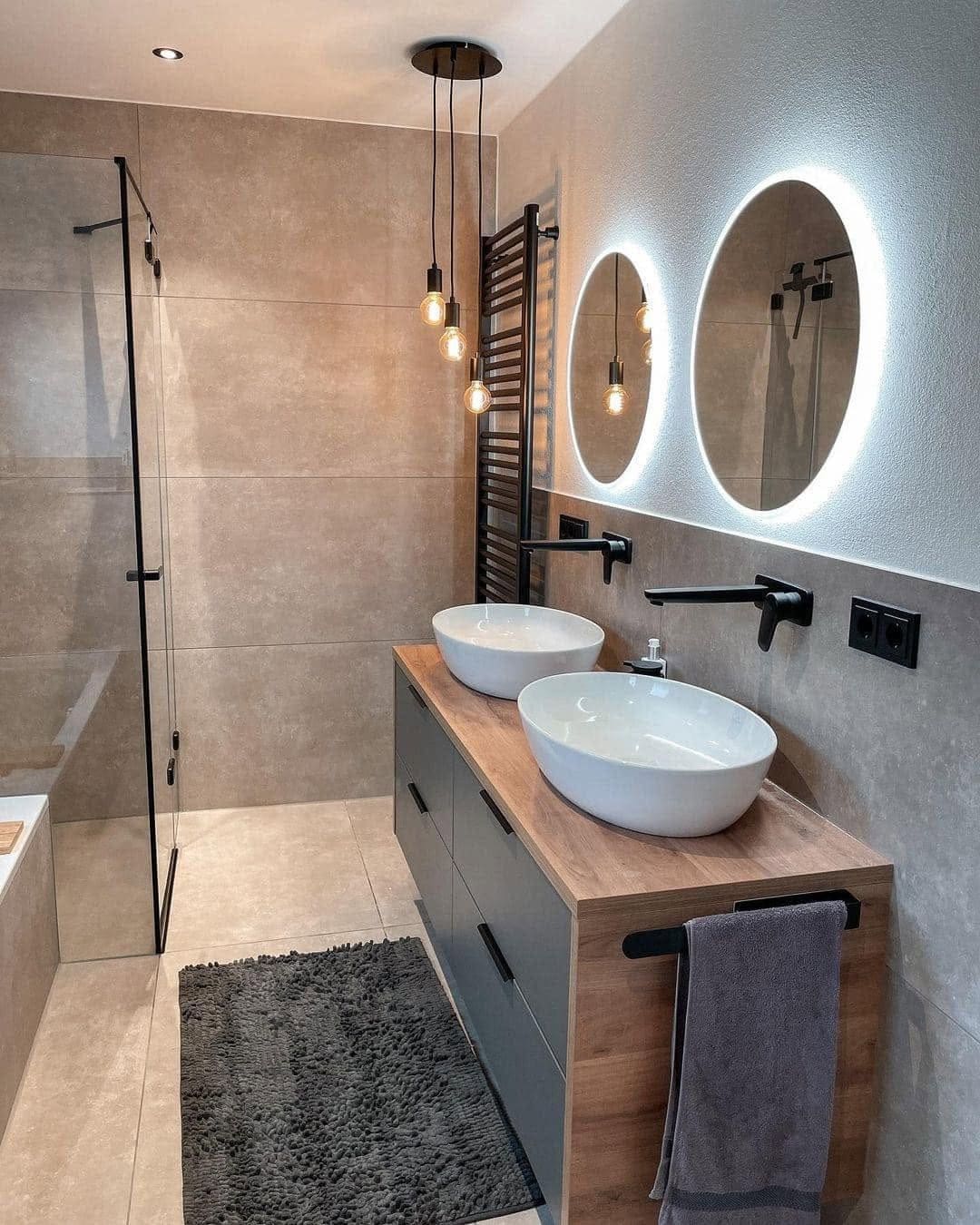 Bathroom with a double vessel-sink vanity, backlit round mirrors and a glass shower panel