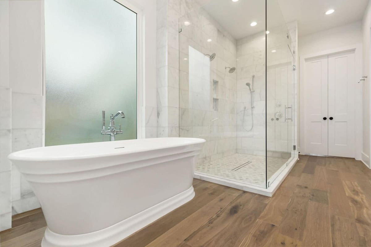 Freestanding soaking tub in front of a frameless glass shower