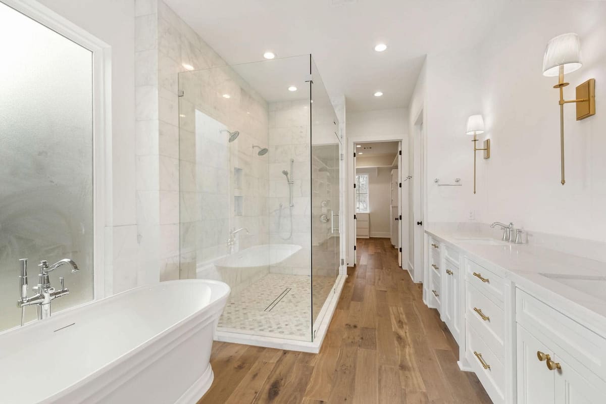 Marble walk-in shower with a glass enclosure and linear drain beside a freestanding tub