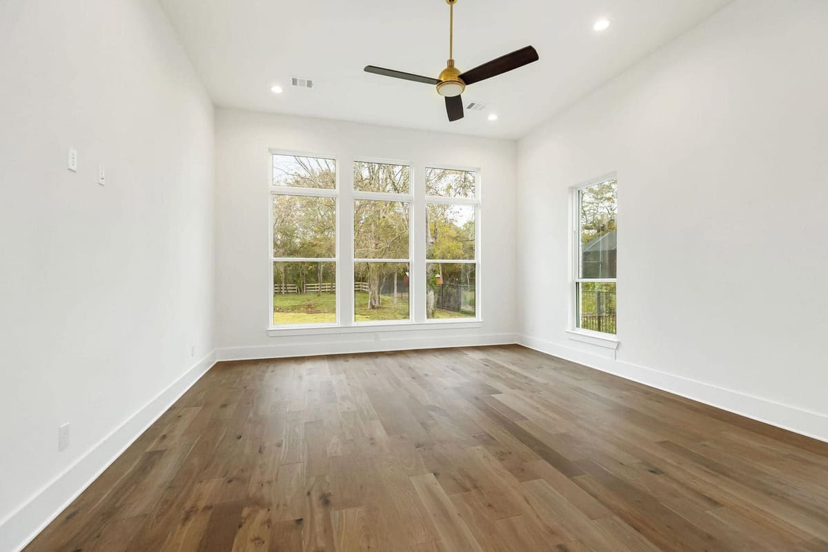Bedroom with wide oak floors, a tall window group and a ceiling fan