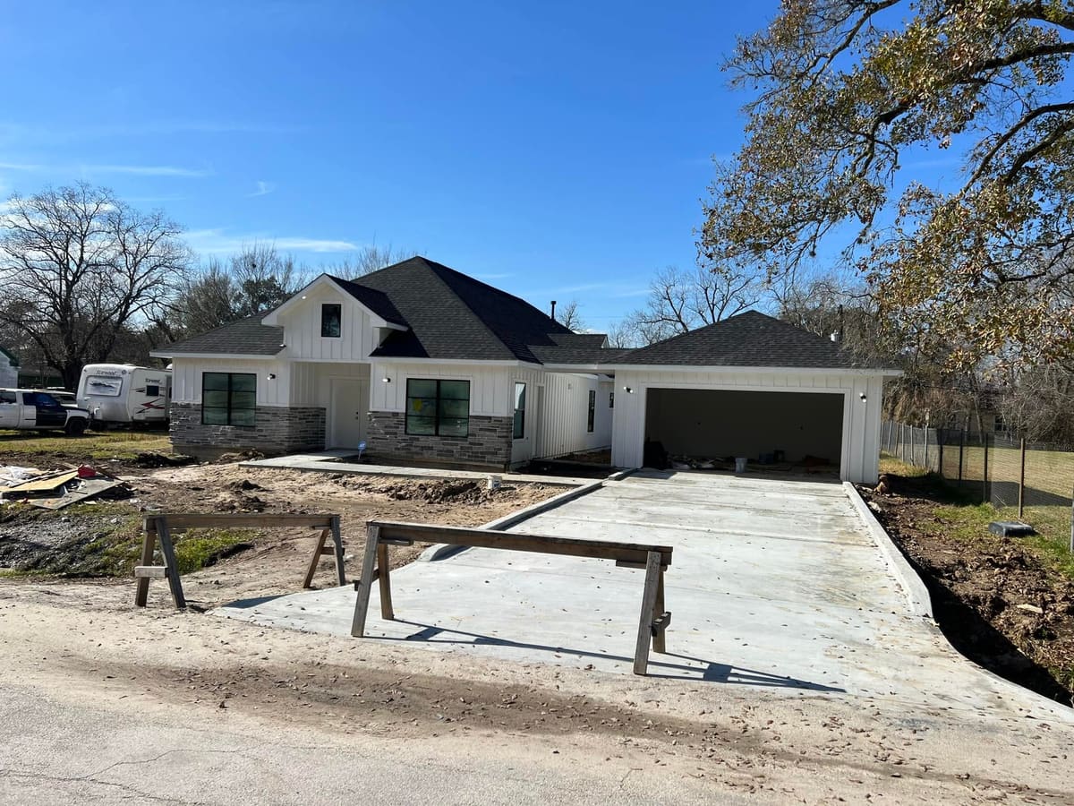 New farmhouse-style home with stone and board-and-batten siding and a freshly poured driveway