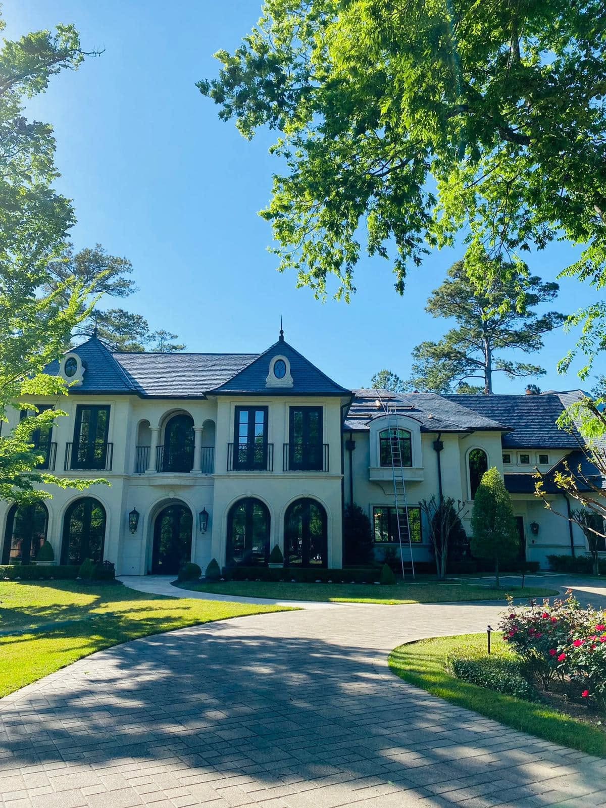 Two-story French-style custom home with arched windows, a slate roof and a curved paver driveway