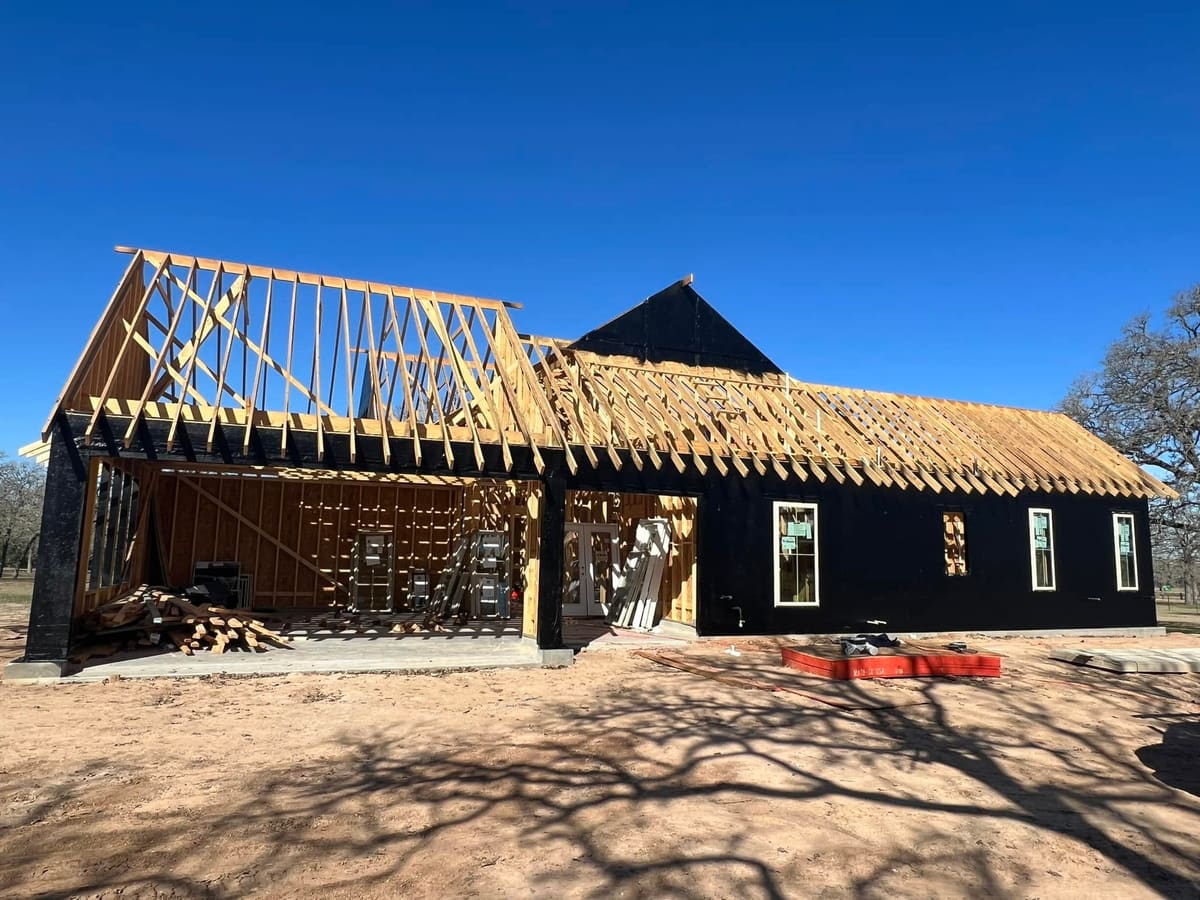 Roof trusses going up on a new home wrapped in black weather barrier