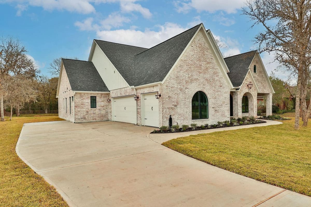 White-brick custom home with steep gables, arched windows and a curved concrete driveway