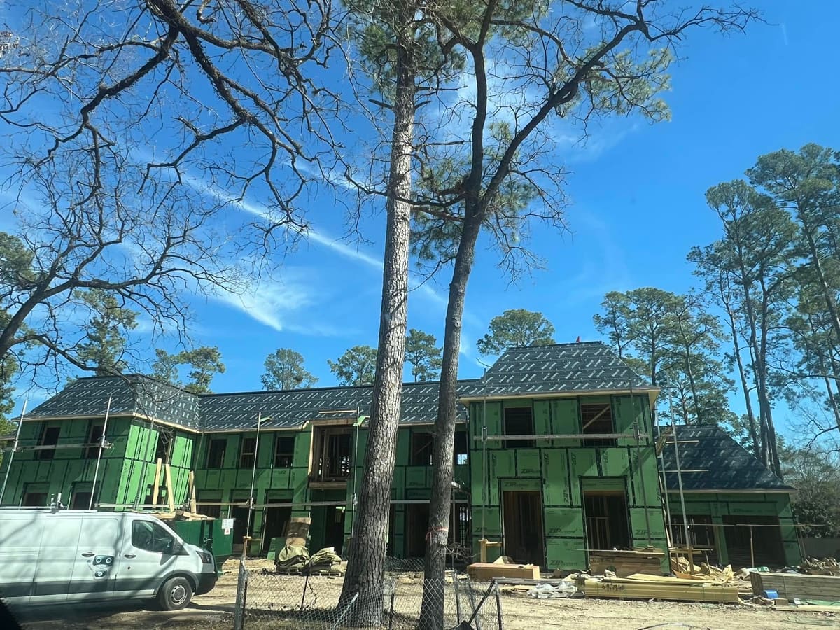 Large two-story home in green sheathing under construction among tall pines