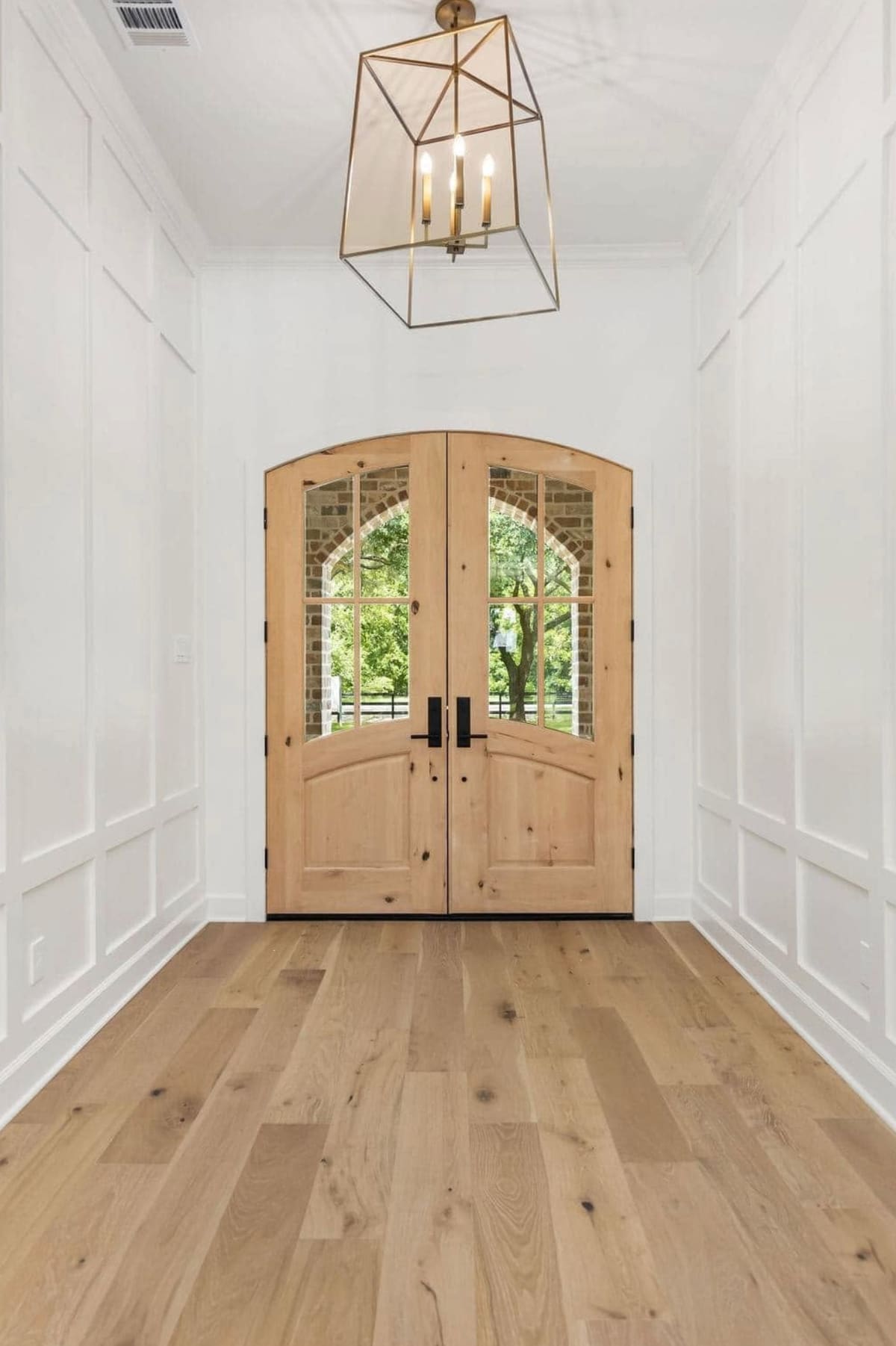 Entry hall with arched double wood doors, paneled walls, a lantern chandelier and oak floors