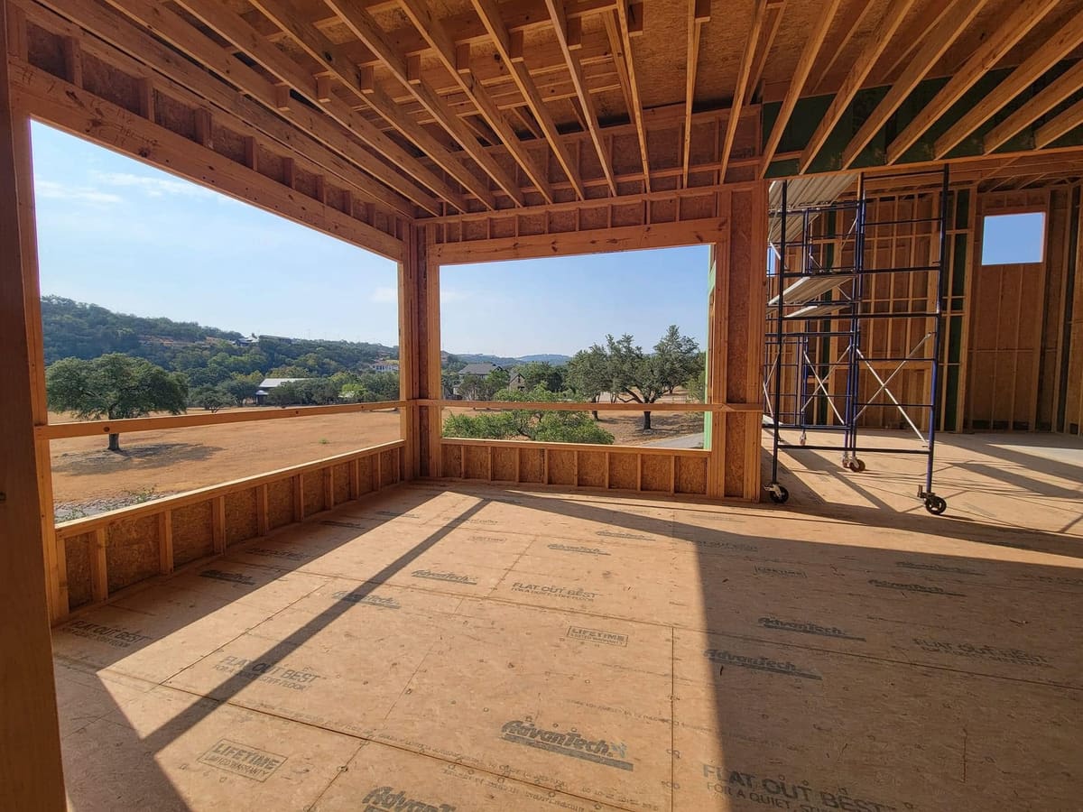 Framed great room with large window openings toward a hillside view