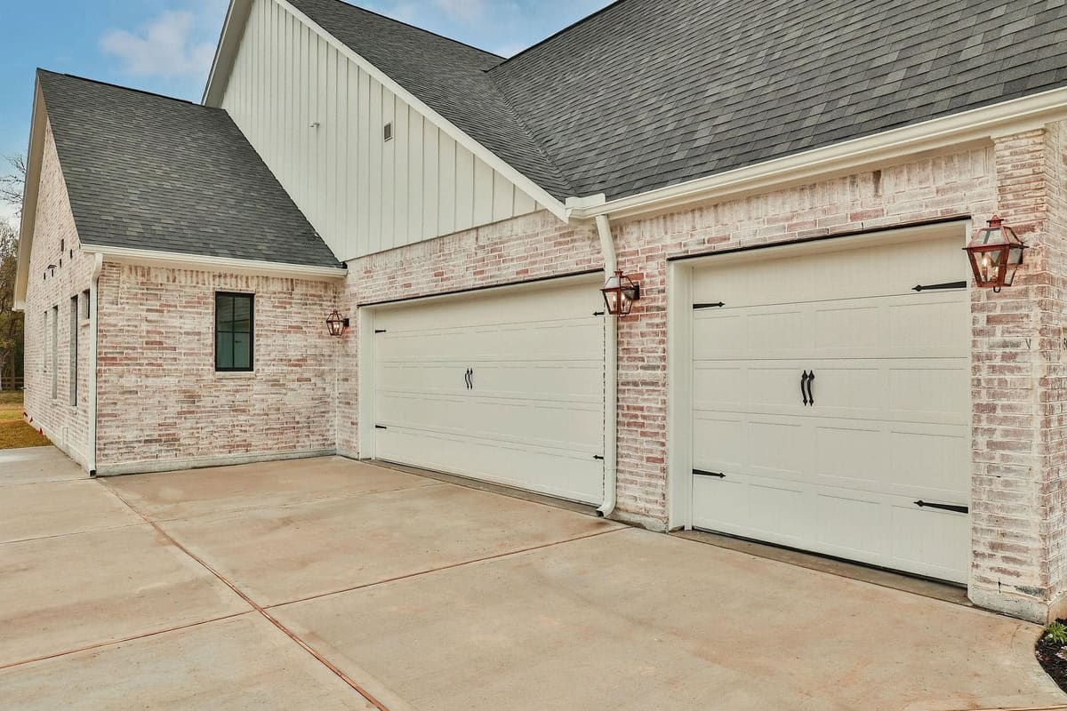 Two carriage-style garage doors set in whitewashed brick with copper lanterns