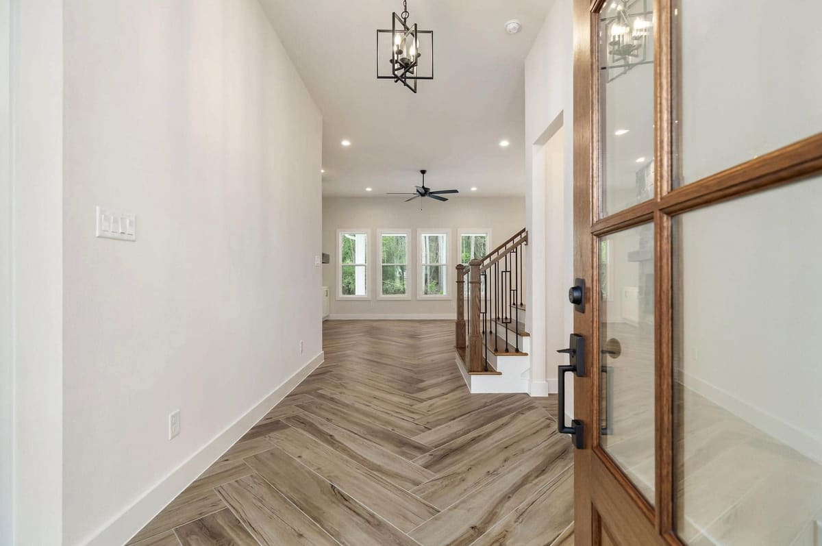 Hallway with herringbone floors leading from the front door to the living area and staircase