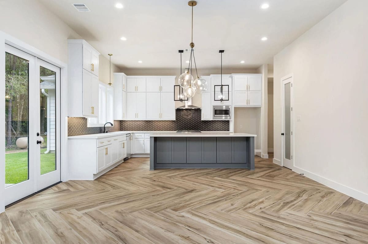 Open kitchen with white cabinets, a gray island, glass pendants and French doors to the yard