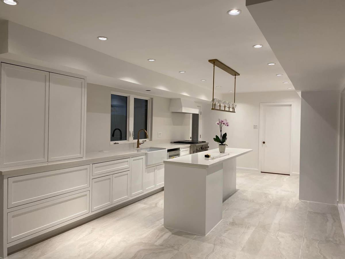 Remodeled kitchen with white flat-panel cabinets, a long island and a brass pendant