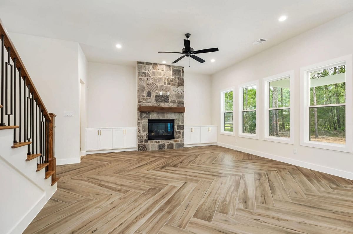 Living room with a stone fireplace, iron-baluster staircase and herringbone wood-look floors