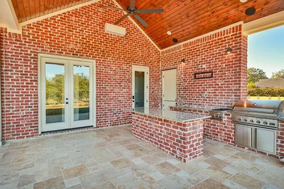 Outdoor kitchen with a brick island, built-in grill and stained wood ceiling under a patio cover