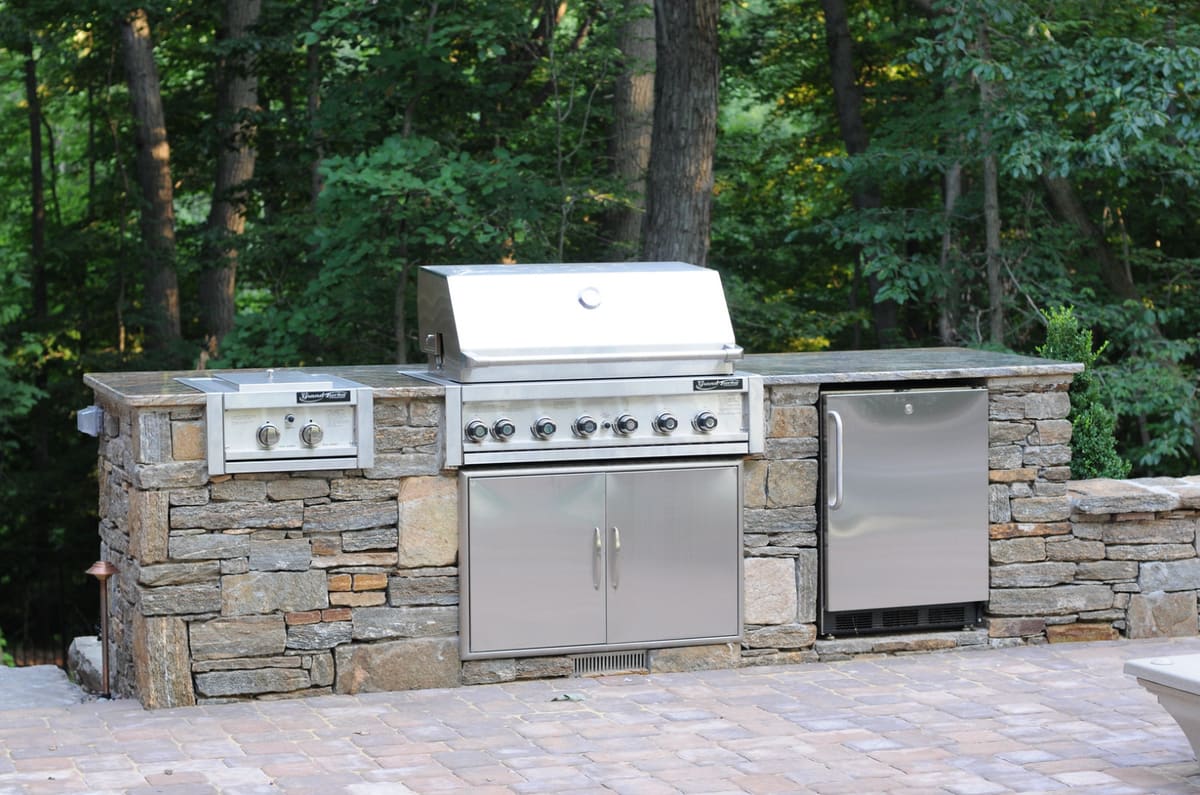 Outdoor kitchen with a stacked-stone island, built-in grill, side burner and refrigerator