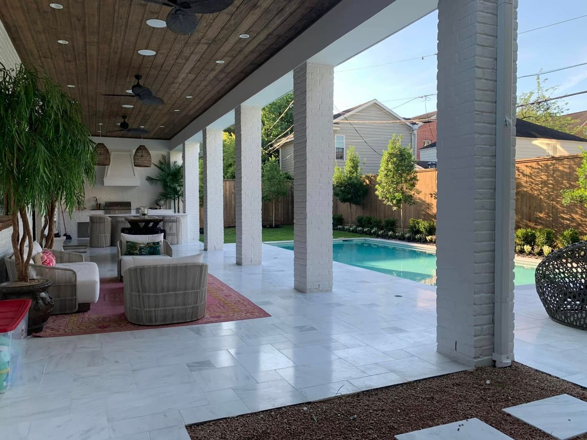 Covered outdoor living area with a stained wood ceiling, fans and lounge seating beside a pool