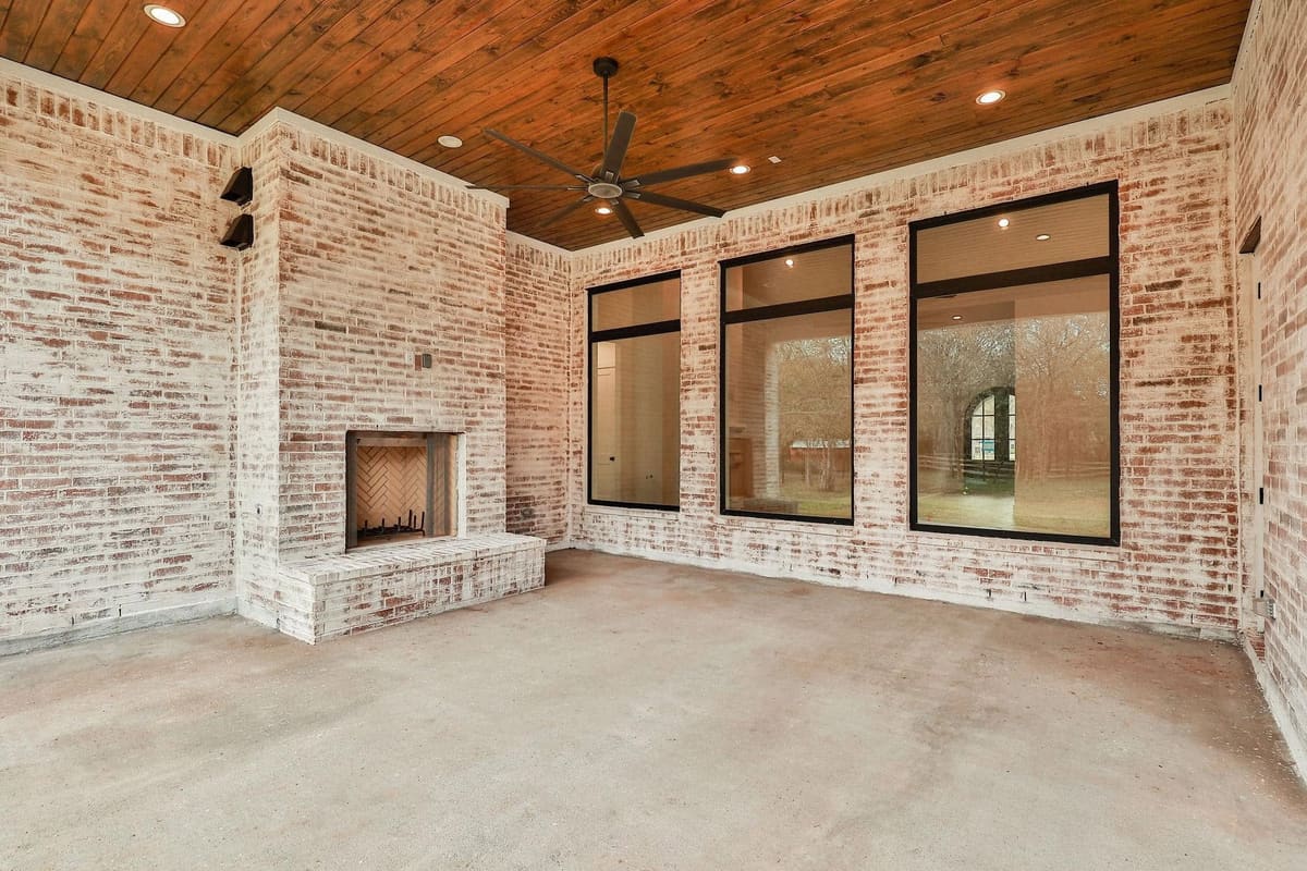 Covered outdoor room with whitewashed brick, a fireplace and a stained wood ceiling