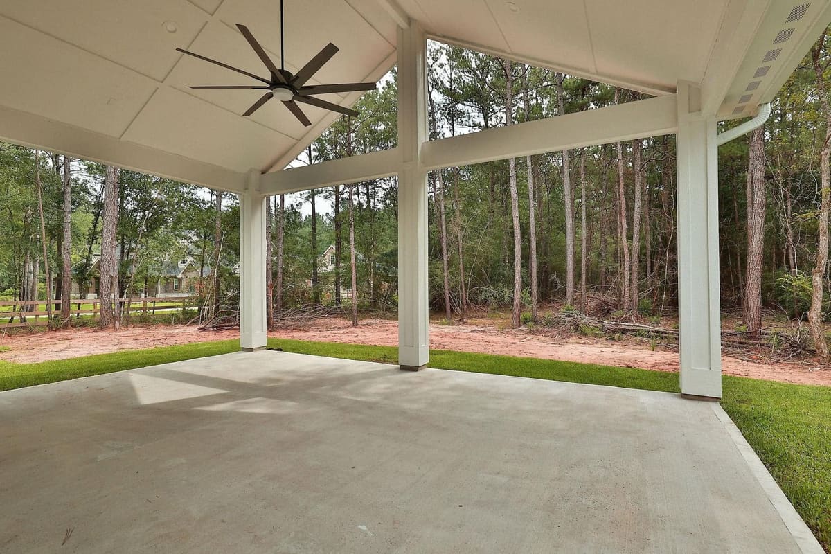 Open gable patio cover with white columns and a ceiling fan facing a wooded yard