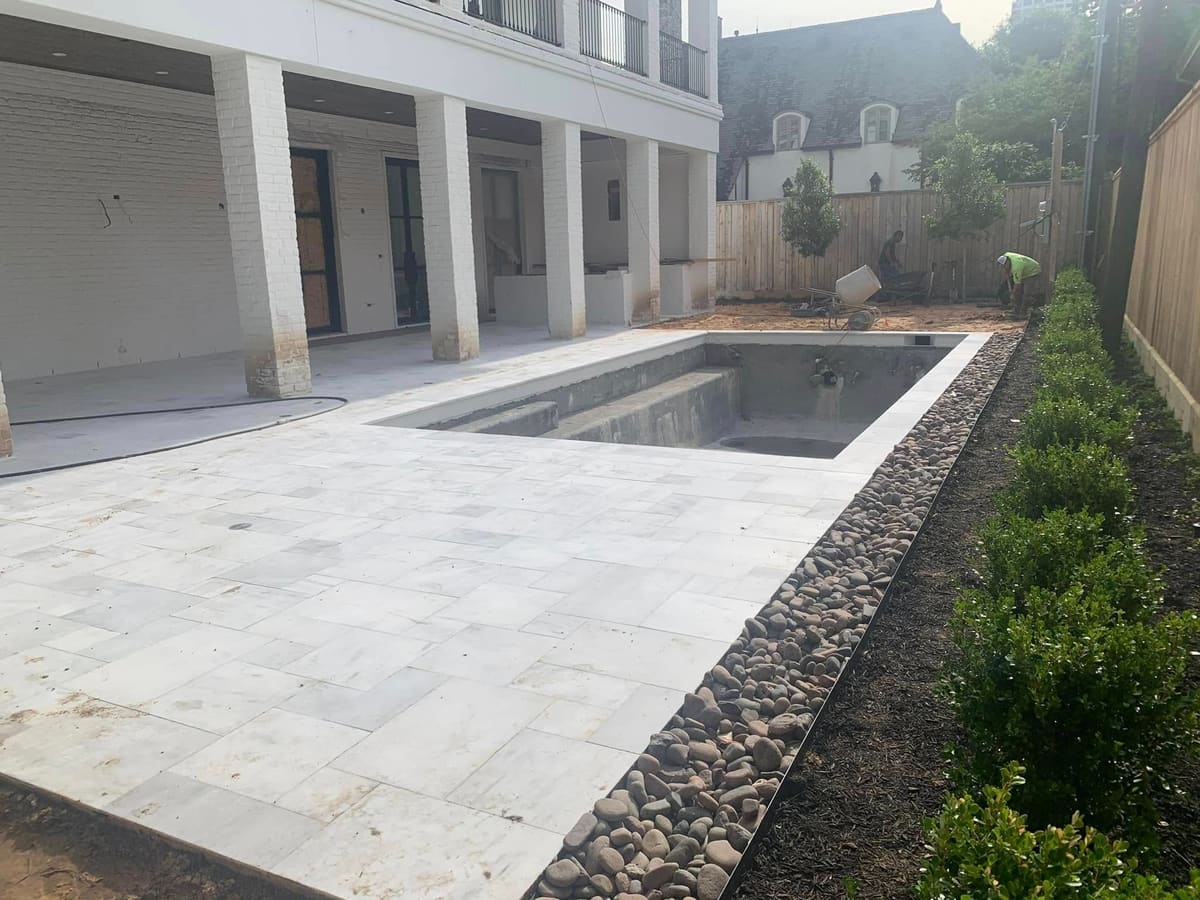 Pool under construction with marble coping and decking beside a covered terrace
