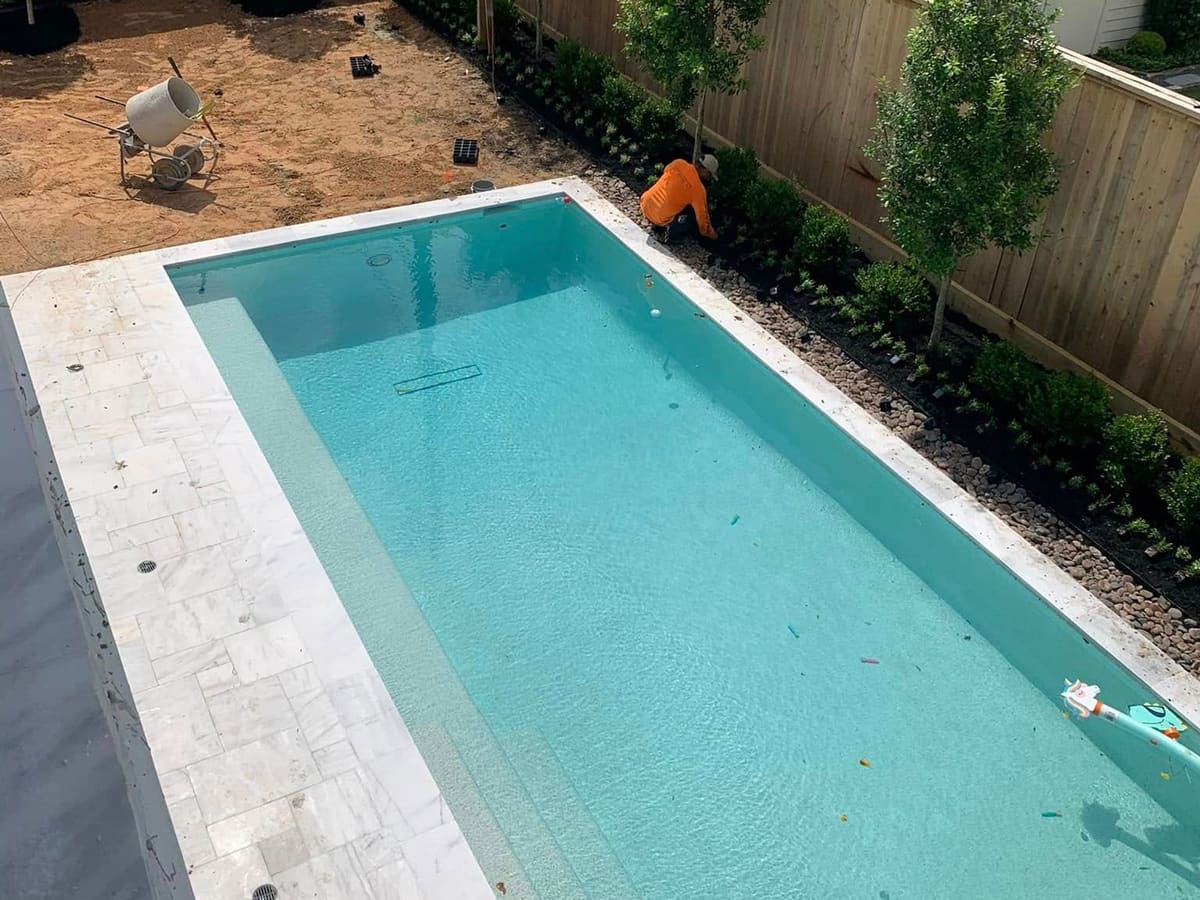 Newly filled rectangular pool with marble coping in a fenced backyard