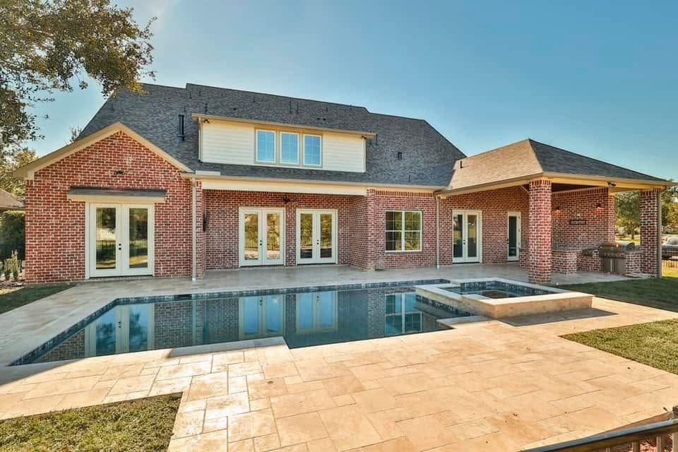 Pool and raised spa with travertine decking behind a red-brick home