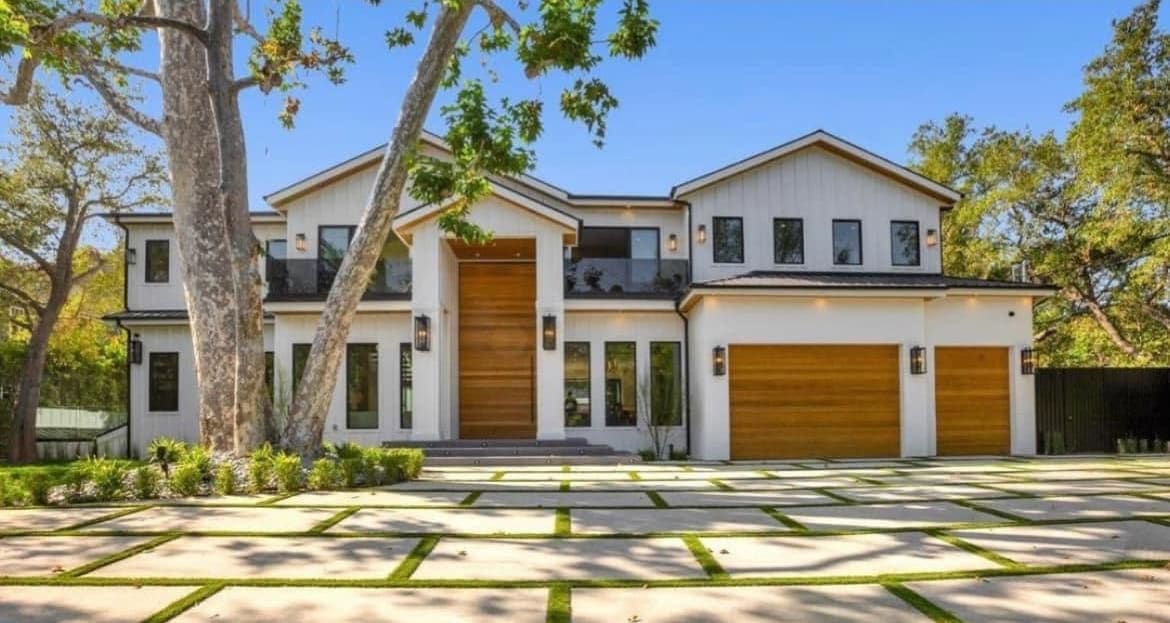 The new two-story home built on the same lot, with wood garage doors and a paver driveway