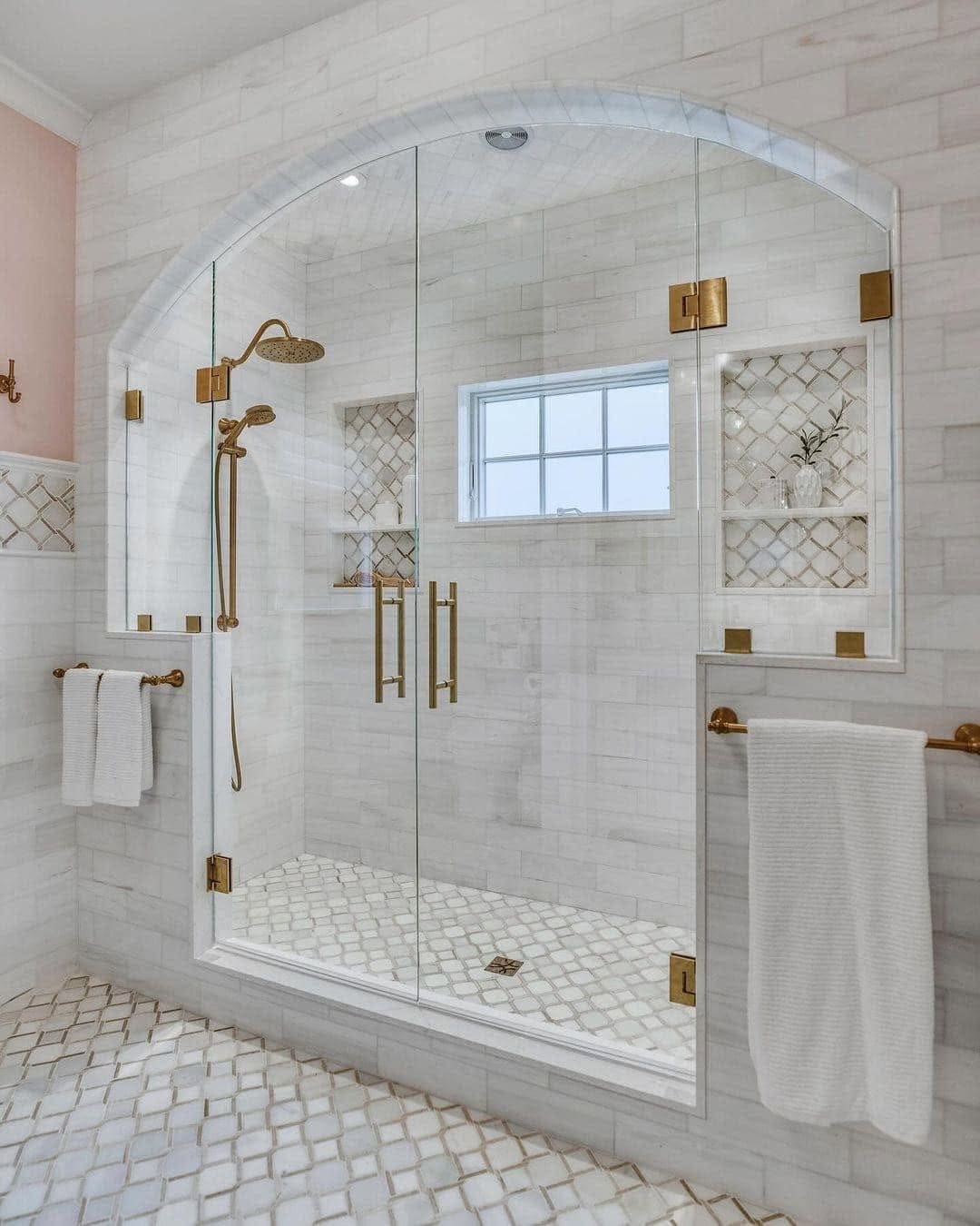 Arched walk-in shower with a frameless glass enclosure, marble tile and brass fixtures