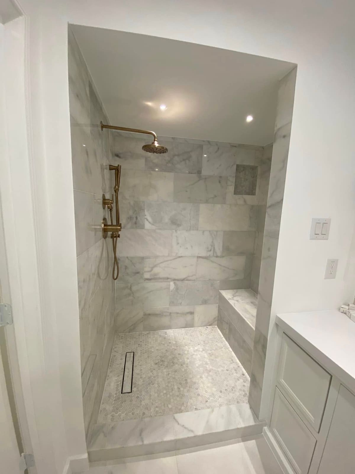 Marble-tiled walk-in shower with a bench, pebble floor and brass fixtures