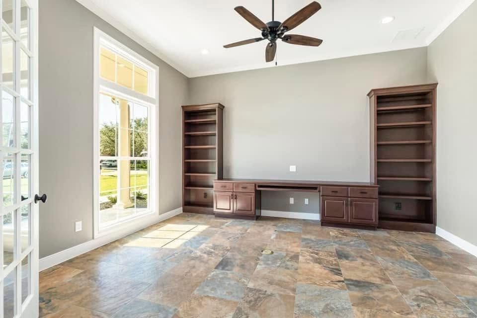 Home office with built-in desk and bookcases and tall windows