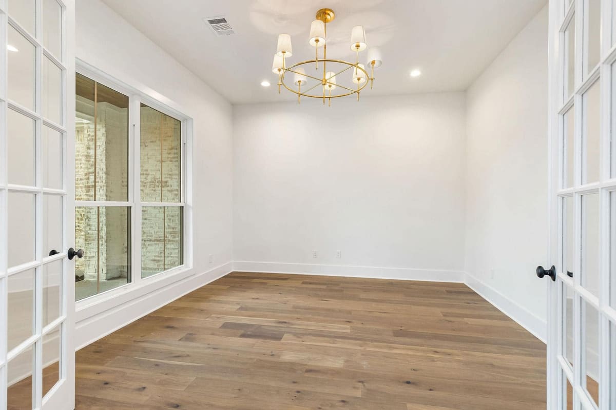 Study with French doors, wide-plank wood floors and a brass chandelier