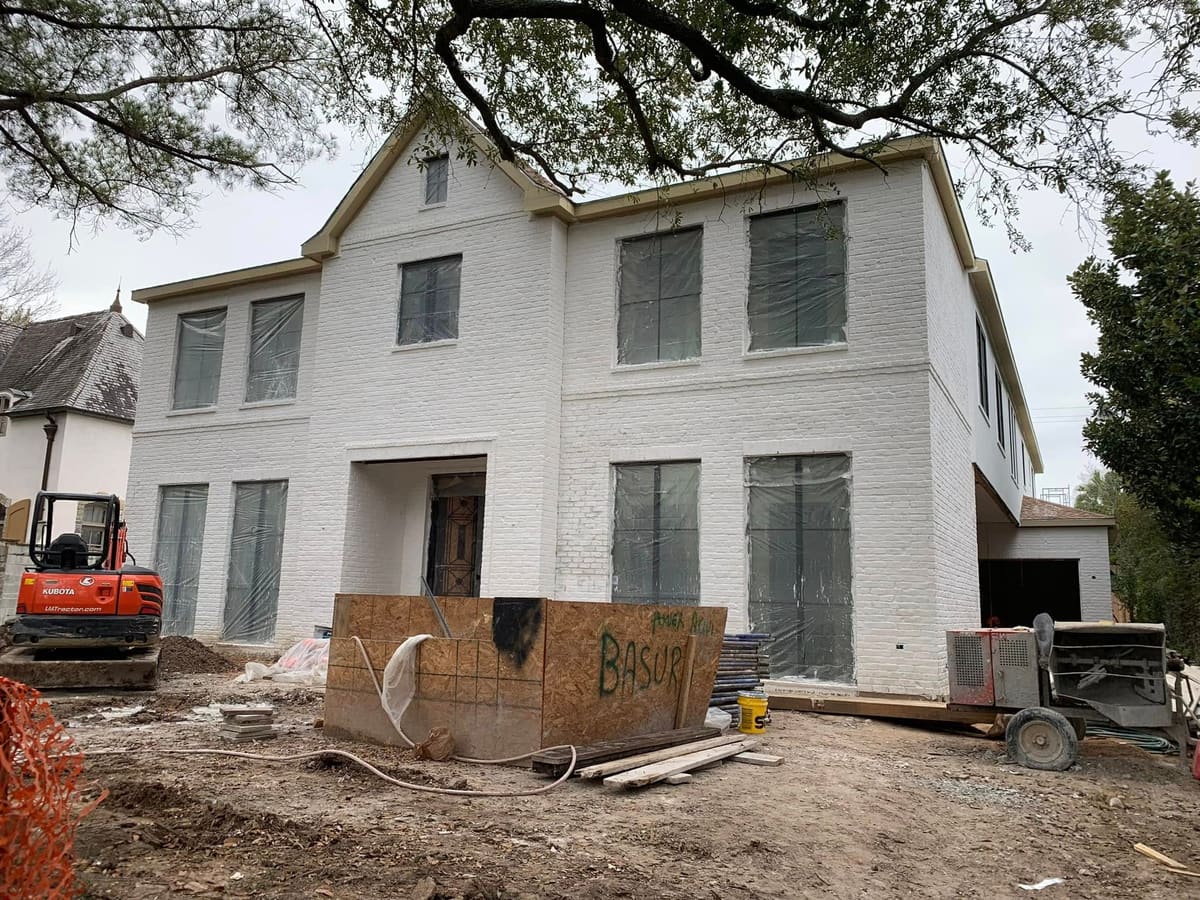 Two-story white-brick home in the finishing stage with equipment on site